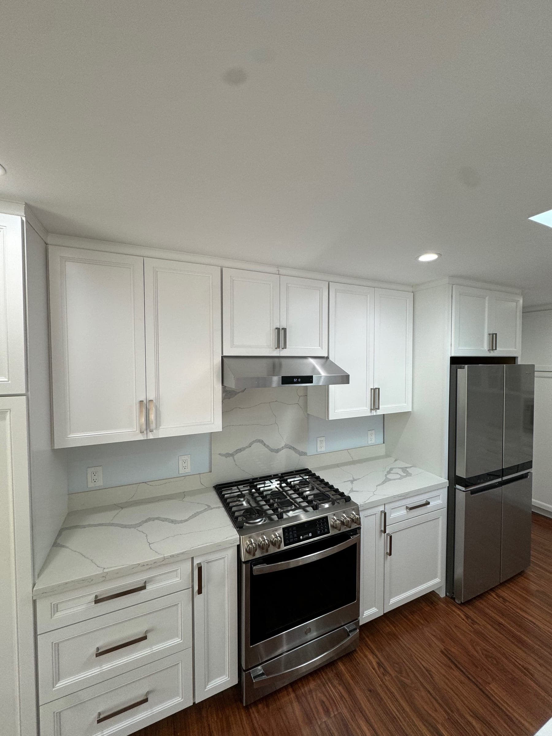 White raised-panel cabinets, quartz backsplash, and stainless range with vent hood in remodeled kitchen